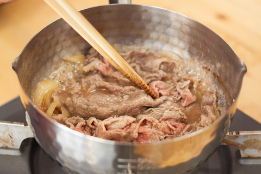 Personne faisant mijoter du bœuf avec des baguettes dans une casserole Yukihira Nabe sur un réchaud à gaz.