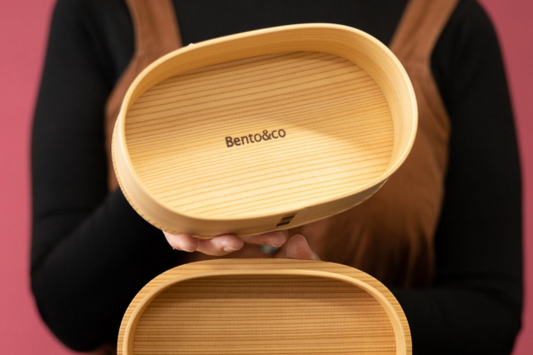Personne tenant un bento en bois de cèdre ouvert avec inscrit à l'intérieur "Bento&co"
