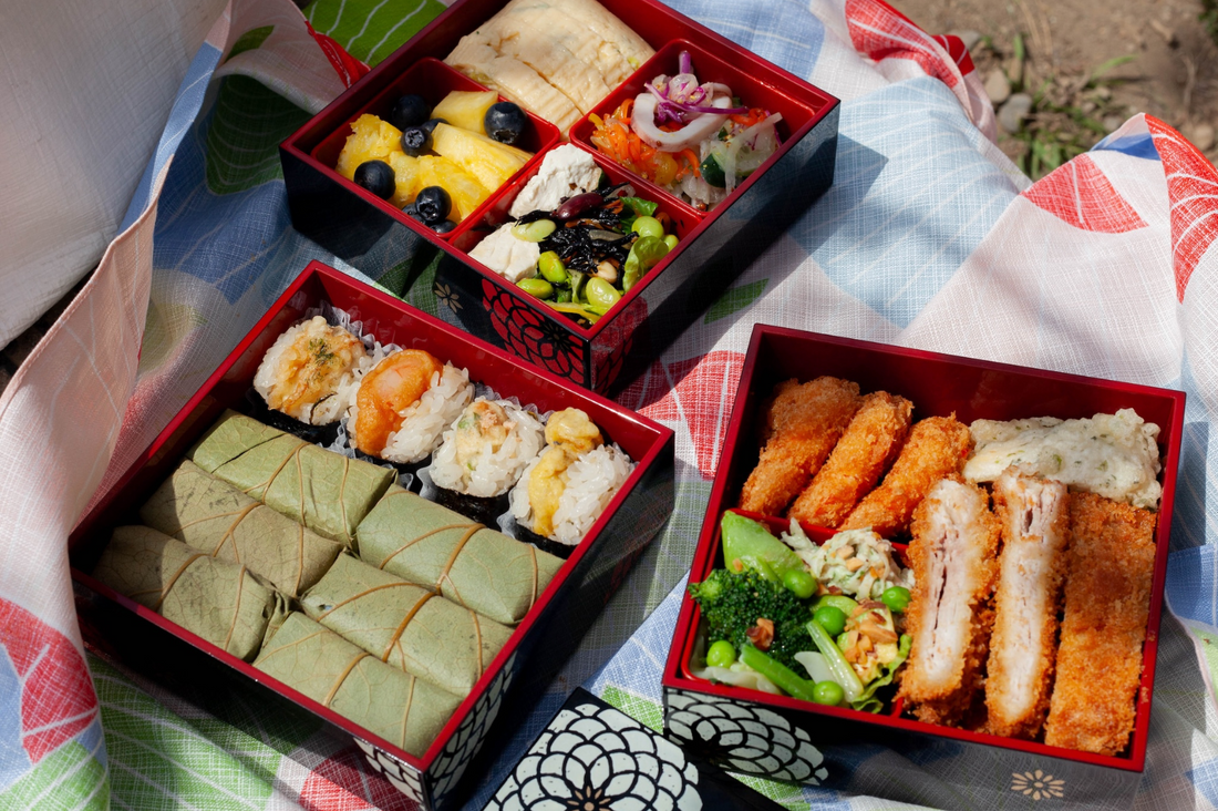 Bento pique-nique noir à 3 étages ouvert sur un furoshiki et rempli de nourriture
