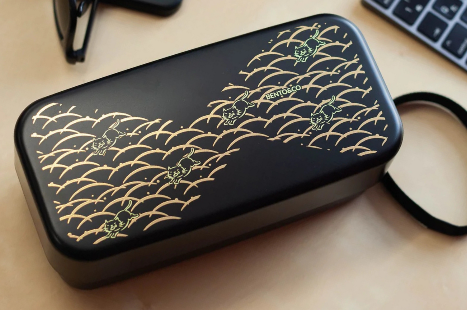 Boîte à bento noir avec des chats jaunes et des vagues dorées sur un bureau en bois
