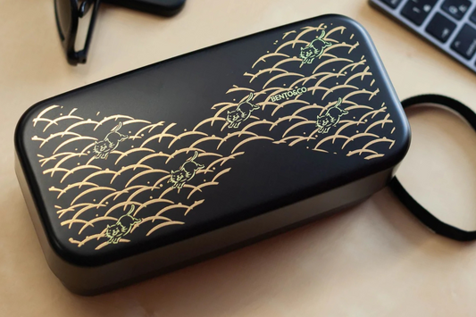 Boîte à bento noir avec des chats jaunes et des vagues dorées sur un bureau en bois
