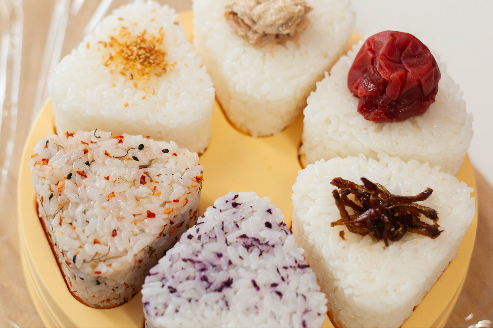 Assortiment d'onigiri avec des garnitures variées sur un moule en plastique jaune orangé
