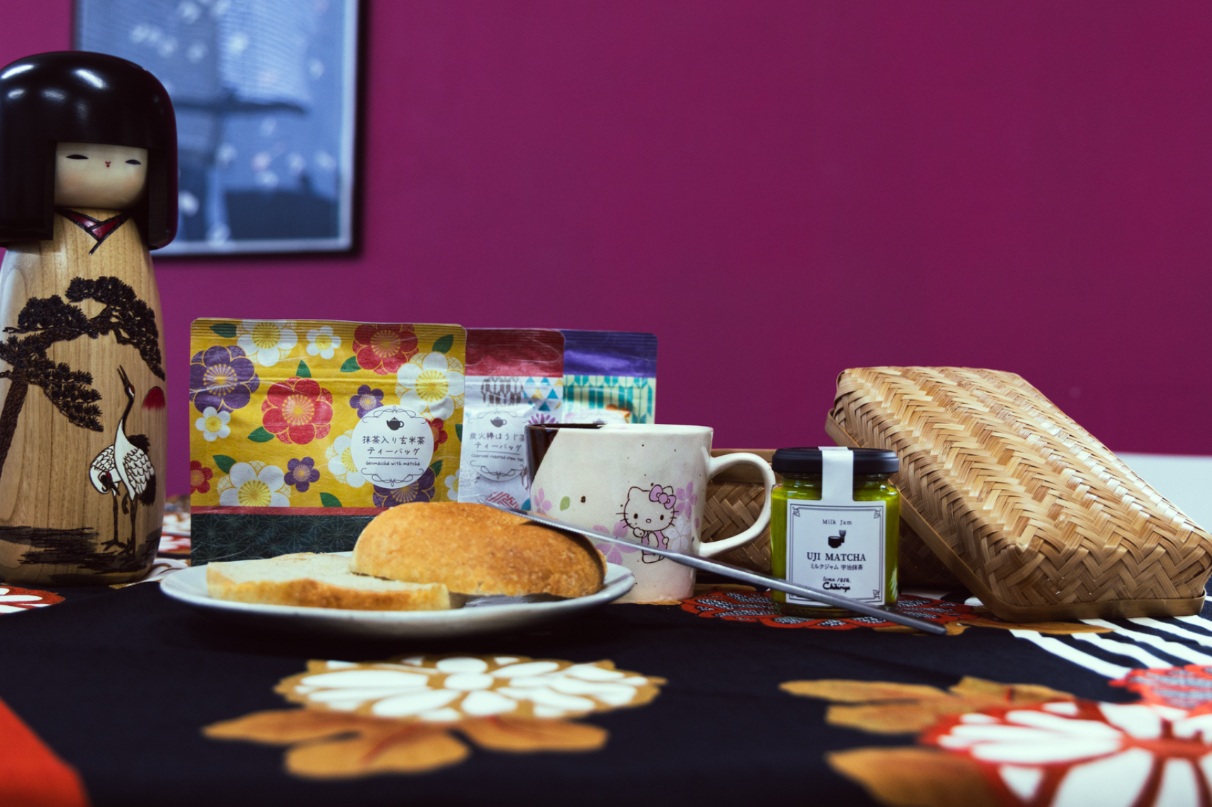 Bagel dans une assiette avec un mug Hello Kitty, de la confiture, des sachets de thé, une poupée Kokeshi et une boîte à bento en bambou tissé
