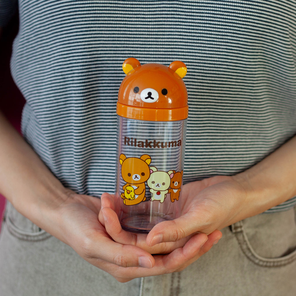 Person holding a transparent bottle with a bear design and 'Rilakkuma' branding.