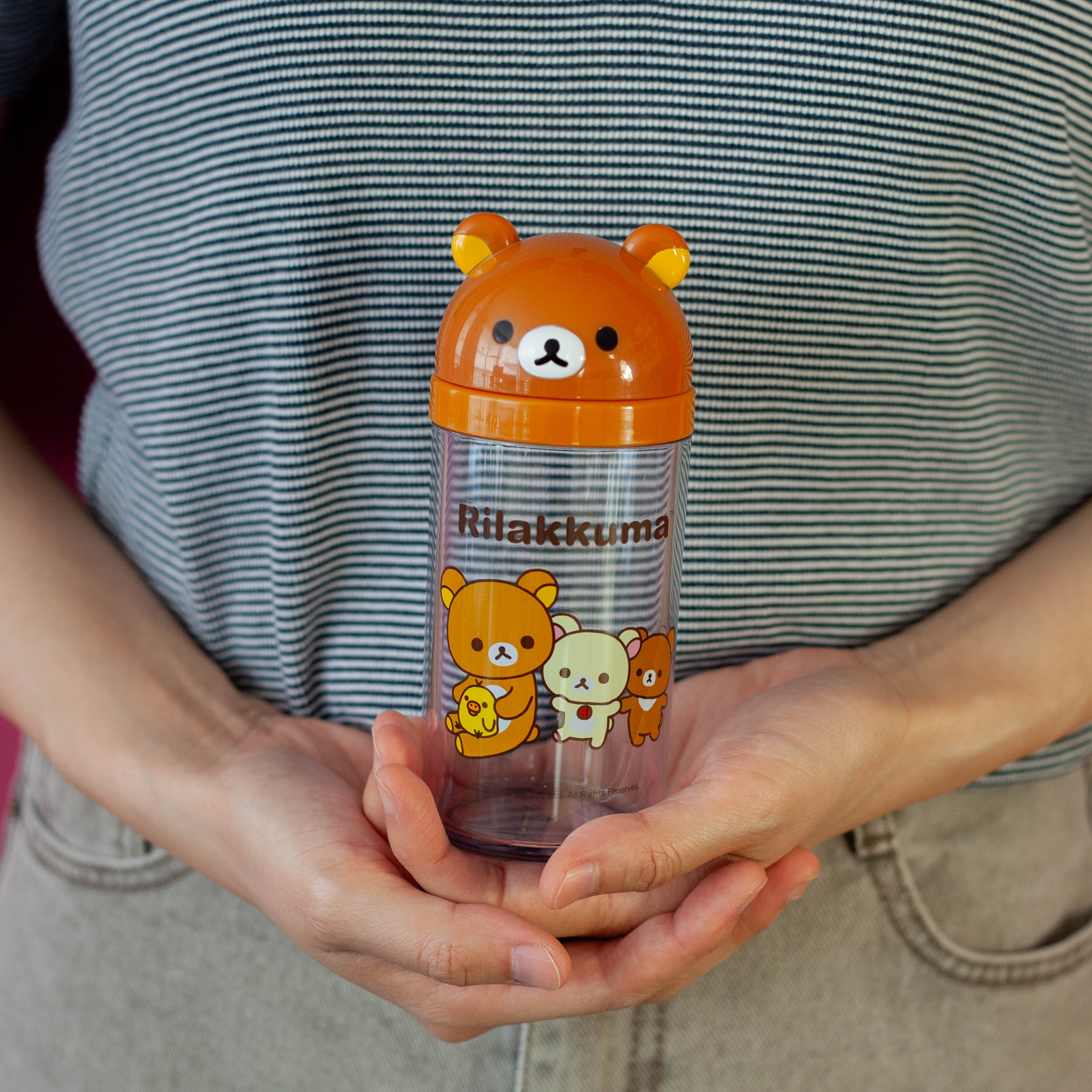 Person holding a transparent bottle with a bear design and 'Rilakkuma' branding.